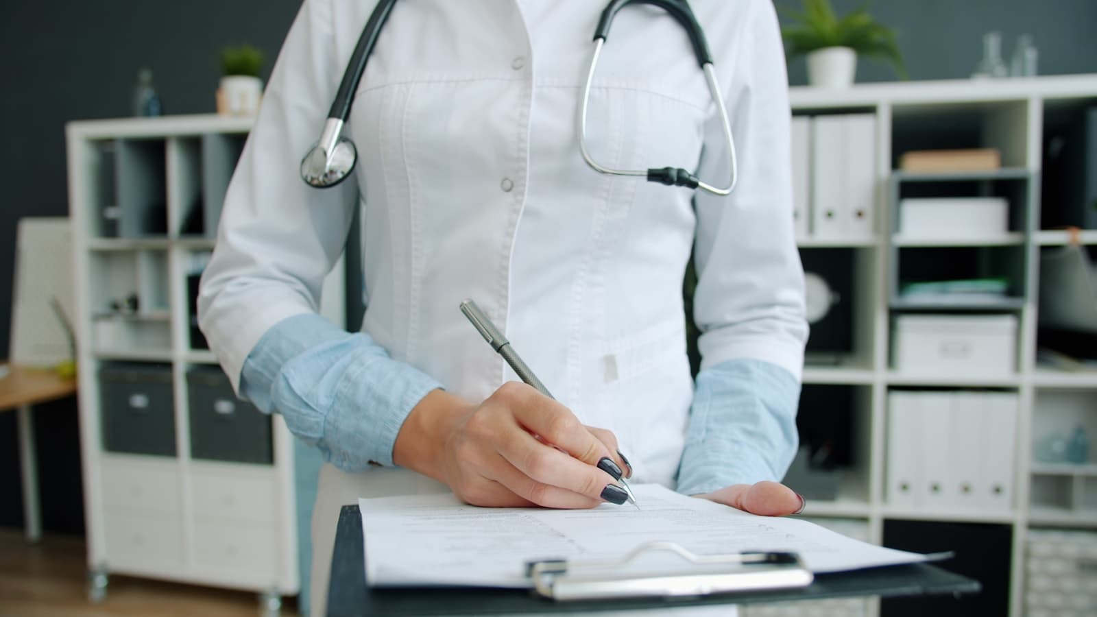 Medical practitioner completing paperwork beside a stethoscope