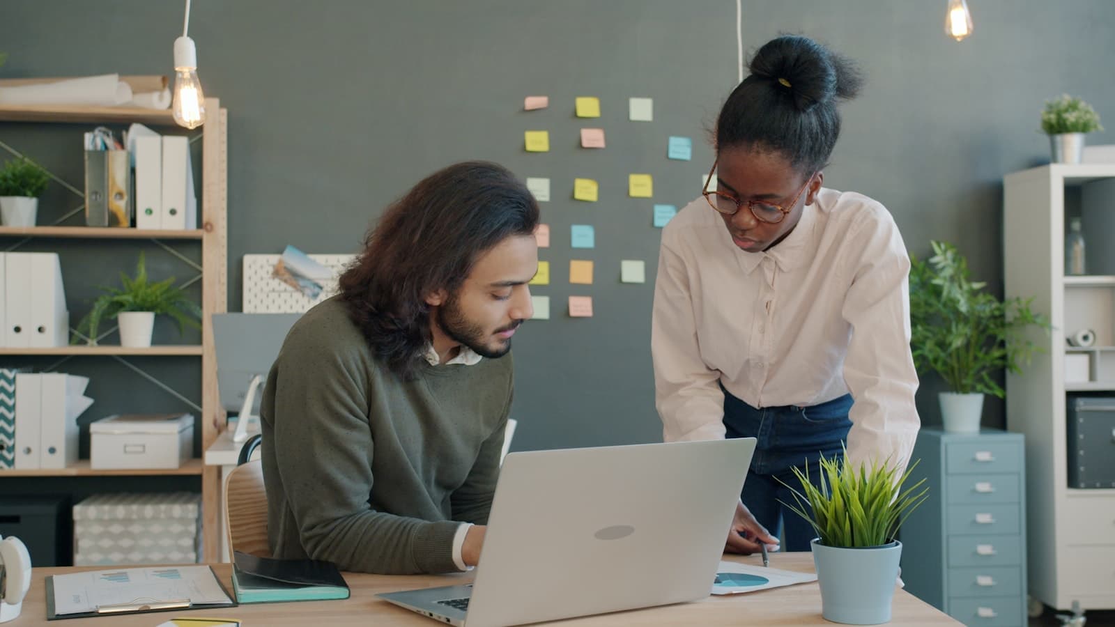 Two colleagues reviewing documents beside a laptop